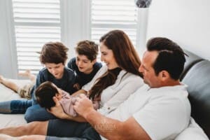 Baby Photography - a family sit on a bed and gaze upon their newborn baby