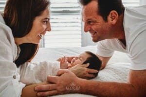 Baby Photography - parents lay on a bed with their baby girl sleeping between them