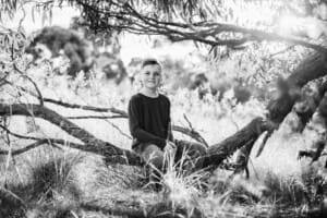 A boy sits in a low tree branch at sunset
