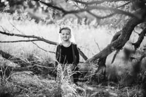 A little girl sits on a low tree branch at sunset