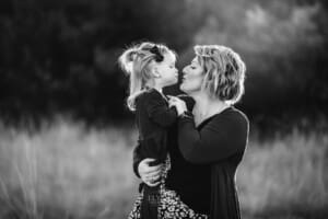 A mother kisses her little girl at sunset