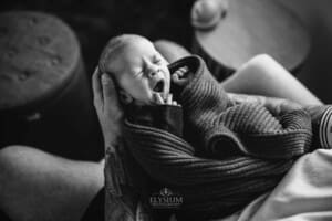 Newborn Photograph - a baby yawns while held in his fathers hands