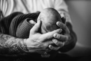 Newborn Photograph - a fathers hands cradle his baby boy's tiny head