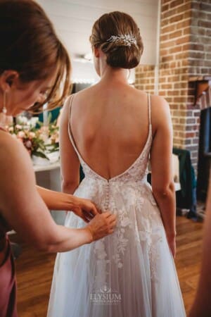 Burnham Grove Wedding - bridesmaid buttons up the back of the bride's dress