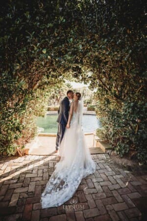 Burnham Grove Wedding - groom kisses his bride under a hedged archway