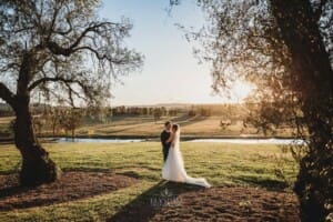 Burnham Grove Wedding - newlyweds cuddle standing between the pepper trees