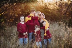parents cuddle their children as they stand in long grass
