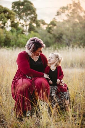A mother cuddles her daughter sitting on a log