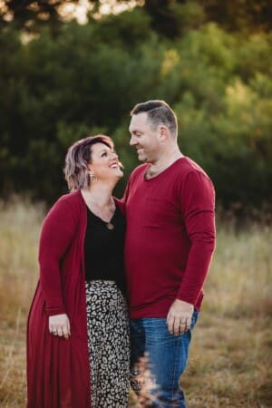 A couple stand cuddling in a grassy field