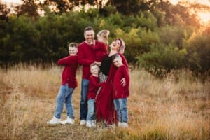 A family cuddle and laugh in a grassy field at sunset