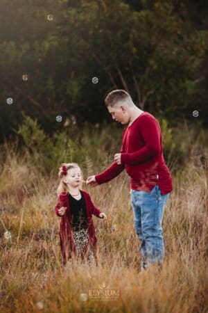 A boy helps his little sister blow bubbles
