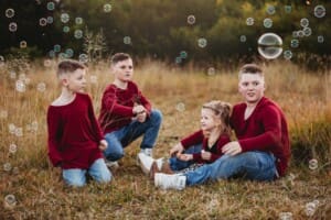 Siblings sit in a grass field and play with bubbles