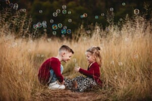 Children sit in long grass and blow bubbles