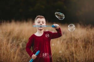 A little boy blows bubbles in a grass field at sunset