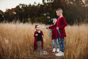 A boy helps his little sister blow bubbles