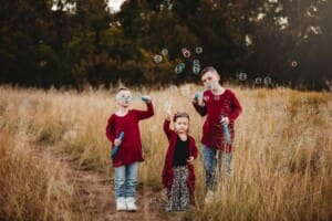 Siblings stand in long grass blowing bubbles