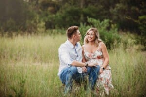 Maternity Photographer - a couple sit on a log in a grassy field