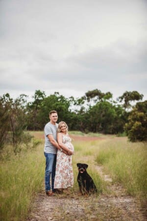 Maternity Photographer - parents cuddle with their puppy in a grass field