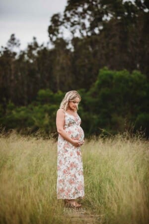 Maternity Photographer - a pregnant woman holds her belly standing in a grassy field
