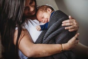 Newborn Photograph - a baby smiles as he is held close to his mum