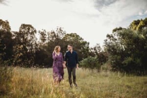 Engagement Photography - a couple hold hands as they walk through a grassy field