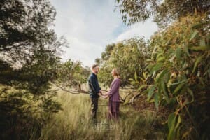 Engagement Photography - a couple standing in long grass hold hands at sunset