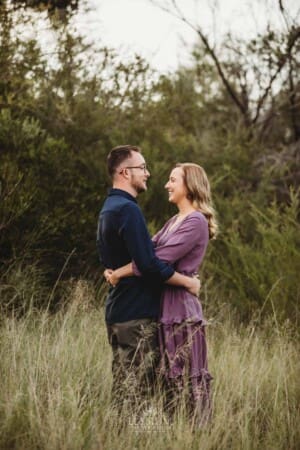 Engagement Photography - a couple cuddle as they stand in long grass