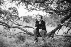A girls sits in the low branch of a tree at sunset