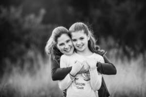 A mother cuddles her daughter in a grassy field