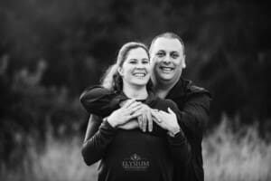 A couple cuddle as they stand in a grass field at sunset