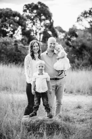 A family stand cuddling in the middle of a grassy field
