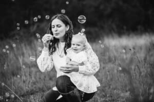 A mother sits with her baby girl and blows bubbles