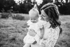 A mother hugs her baby girl in a field at sunset