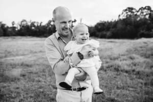 A dad holds his little girl in a grass field at sunset