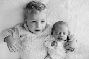A little boy lays on a bed cuddling his baby sister