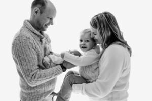 A family hold their newborn baby between them against a bright window