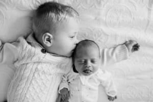 A little boy kisses his newborn baby sister on the head