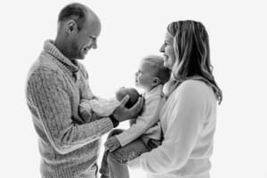 A family hold their newborn baby between them against a bright window