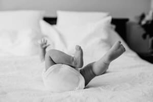 A newborn baby with her legs up laying on a white bed