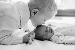 A little boy kisses his newborn baby sister on the head
