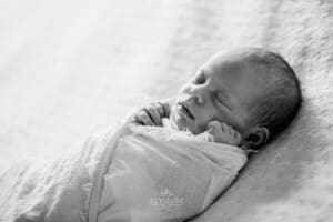 A newborn in a white wrap lays sleeping on a white backdrop