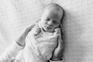 A newborn in a white wrap, mothers hands hold her baby