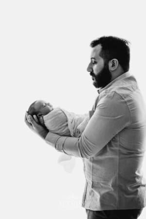 A father stand against a bright window holding his newborn