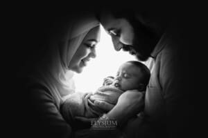 Parents stand with heads together holding their newborn between them