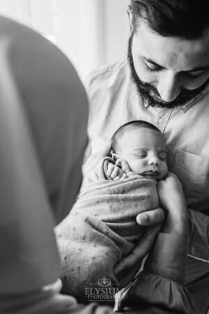 A father holds and looks down at his newborn in his arms