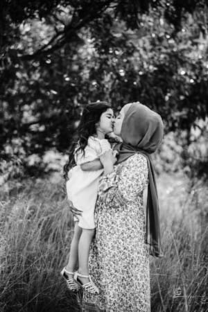 A mother hugs her little girl as they stand in long grass