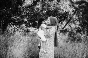 A mother hugs her little girl as they stand in long grass