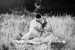 A couple cuddle as they sit in a grassy field at sunset
