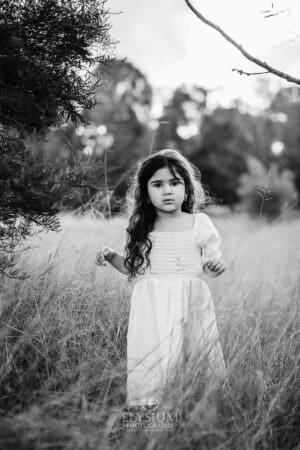 A little girl in a white linen dress stands in long grass