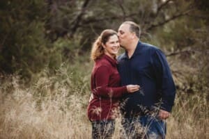 A man kisses his partner on the head as they stand in long grass